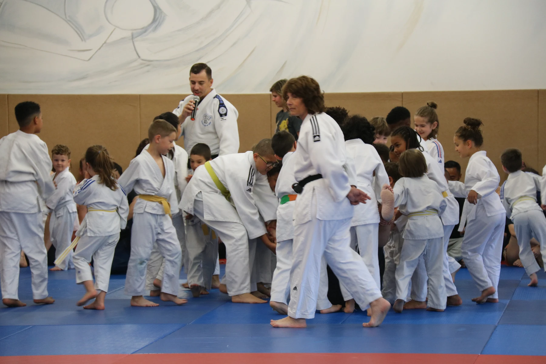 Deux judokas exécutant une technique de projection, sous le regard attentif de jeunes enfants assis au fond.