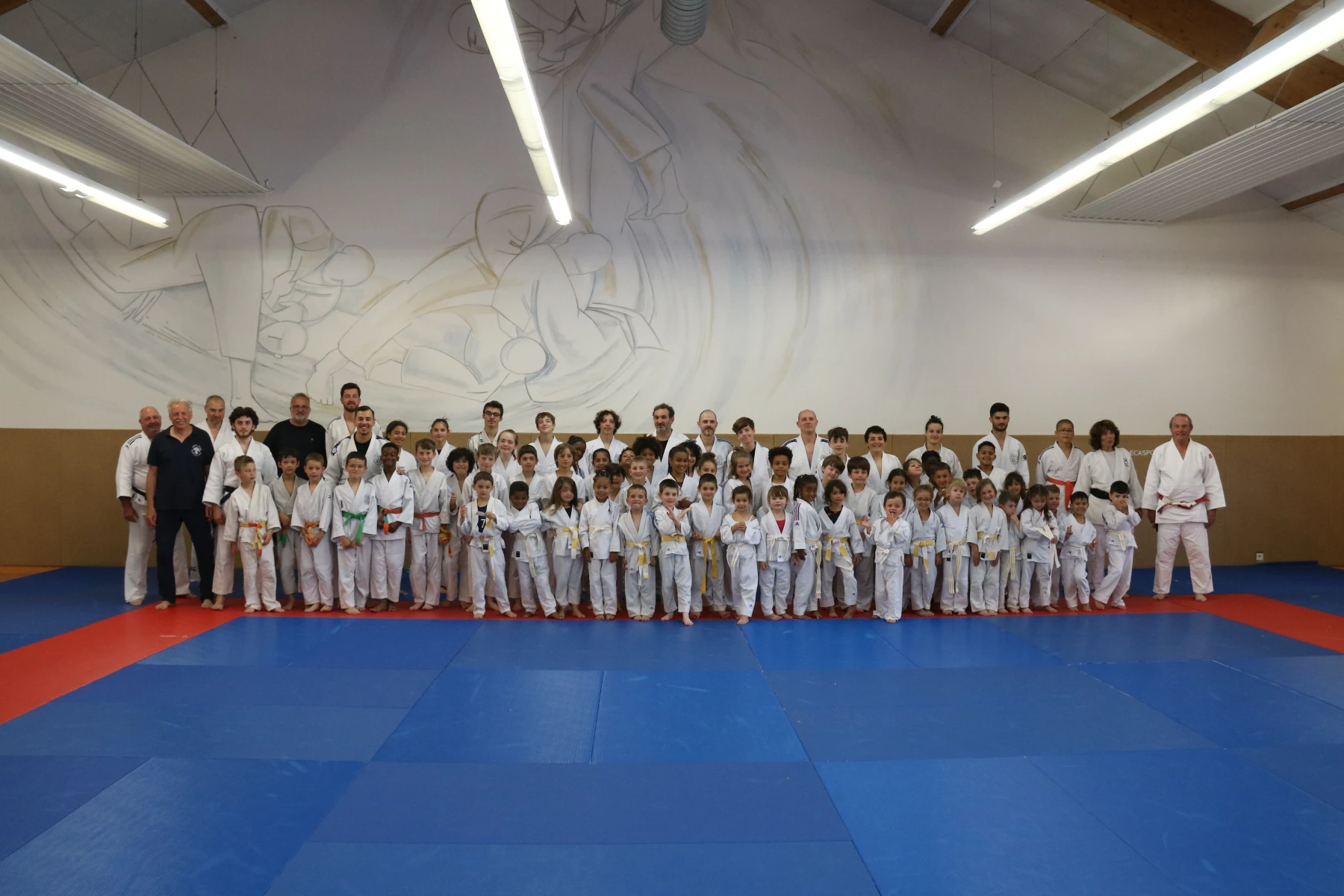 Un pratiquant de judo exécutant un mouvement de projection pendant une démonstration au dojo sous le regard des enfants assis.