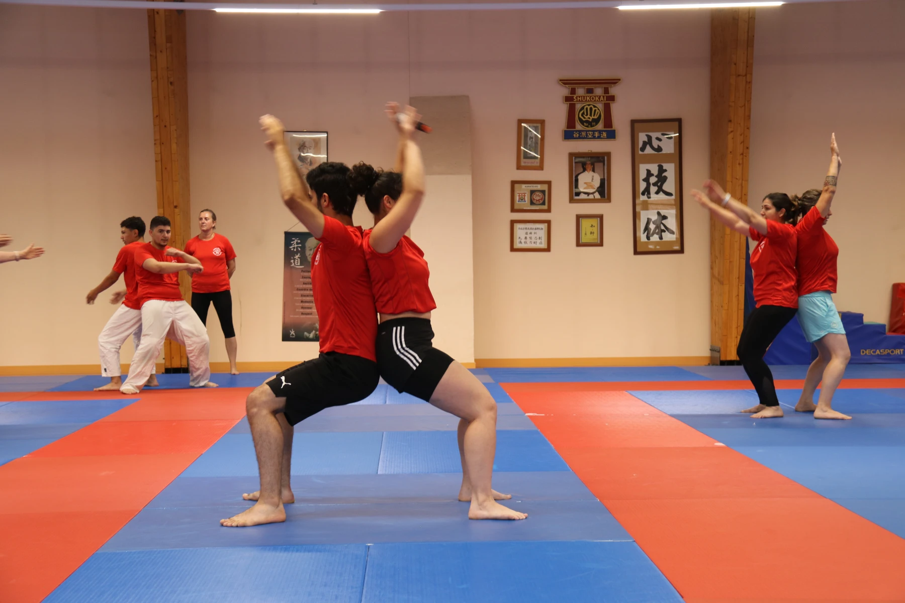 Deux animateurs en t-shirt rouge exécutent une chorégraphie dos à dos pendant un spectacle au dojo.