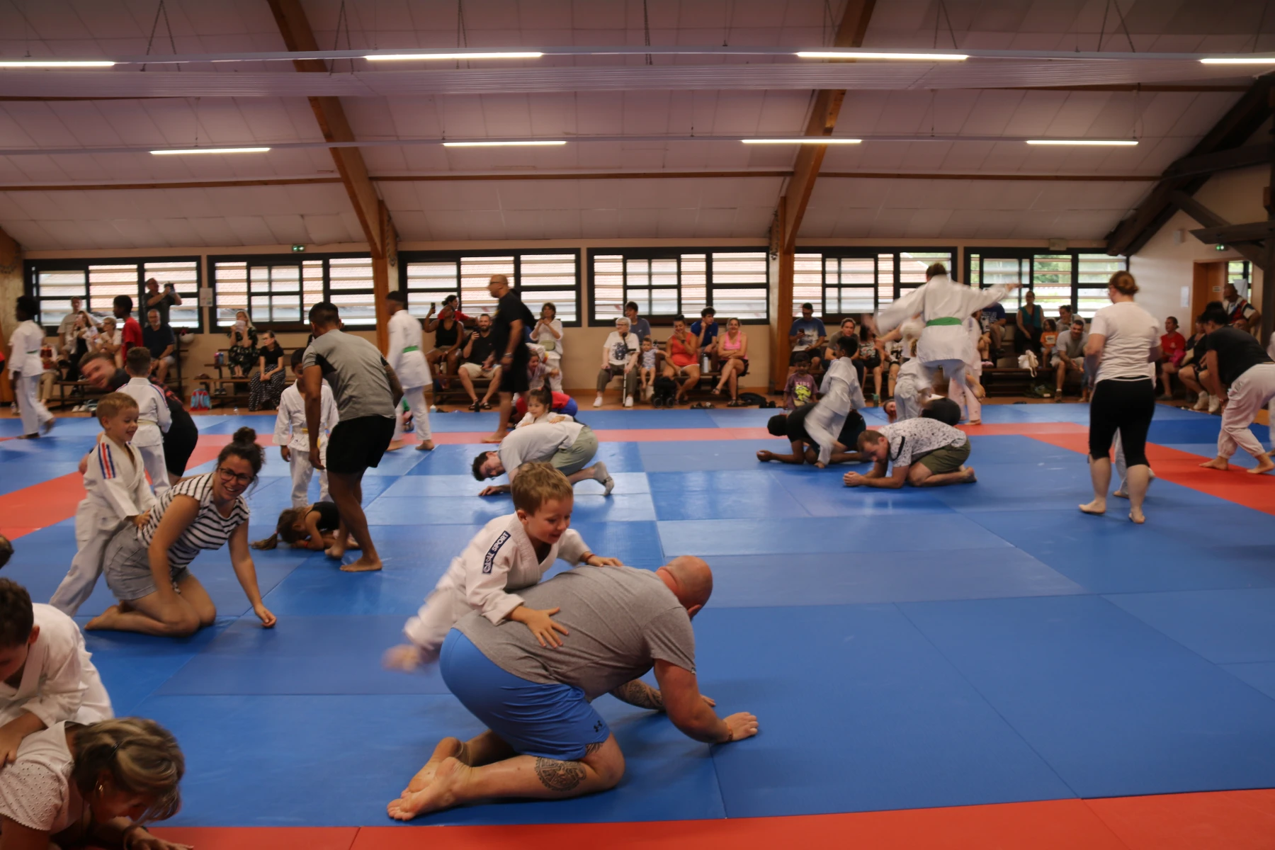 Enfants et parents chahutent joyeusement à genoux sur les tatamis pendant un jeu de l'activité familiale.