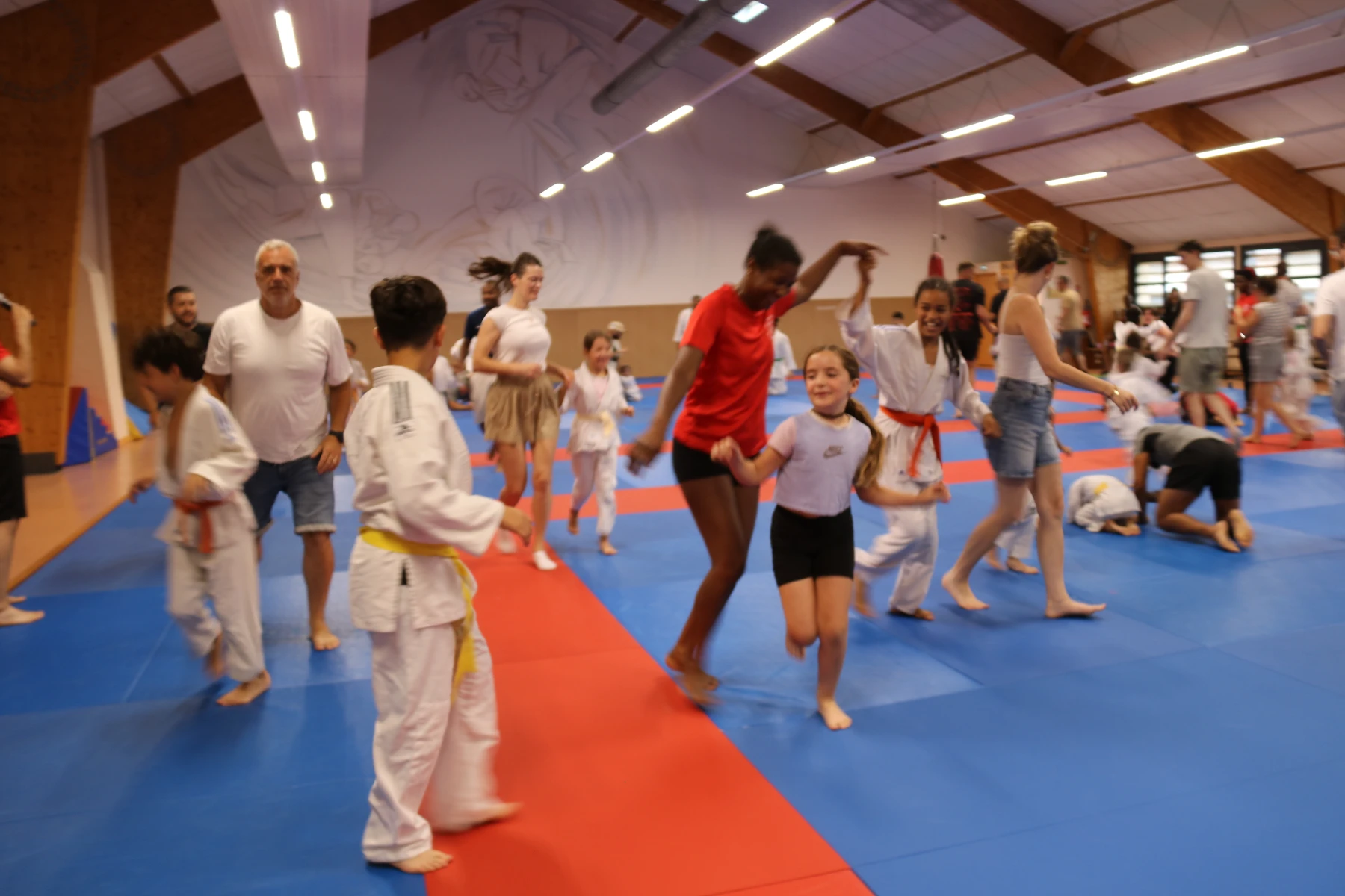 Judokas et familles courent et dansent ensemble sur le tatami au cours d'un jeu collectif plein d'énergie.