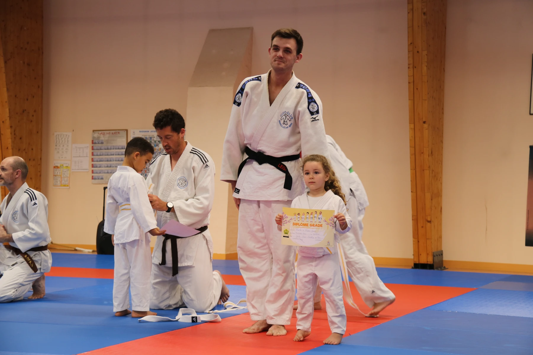 Un assistant ceinture noire pose fièrement aux côtés d'une petite judoka tenant son diplôme de grade.