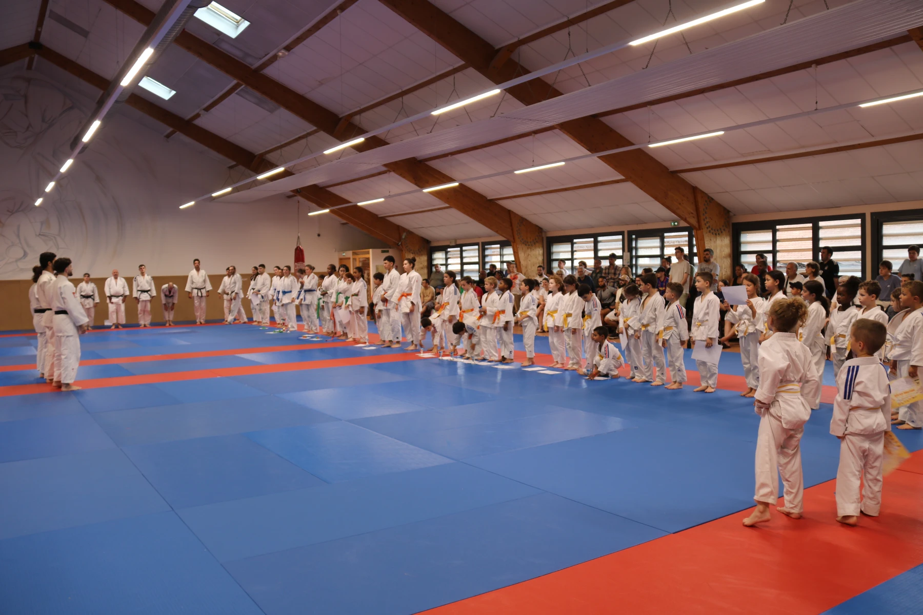 Tous les judokas alignés autour du tatami pour le salut de fin d'événement, parents et enfants réunis.