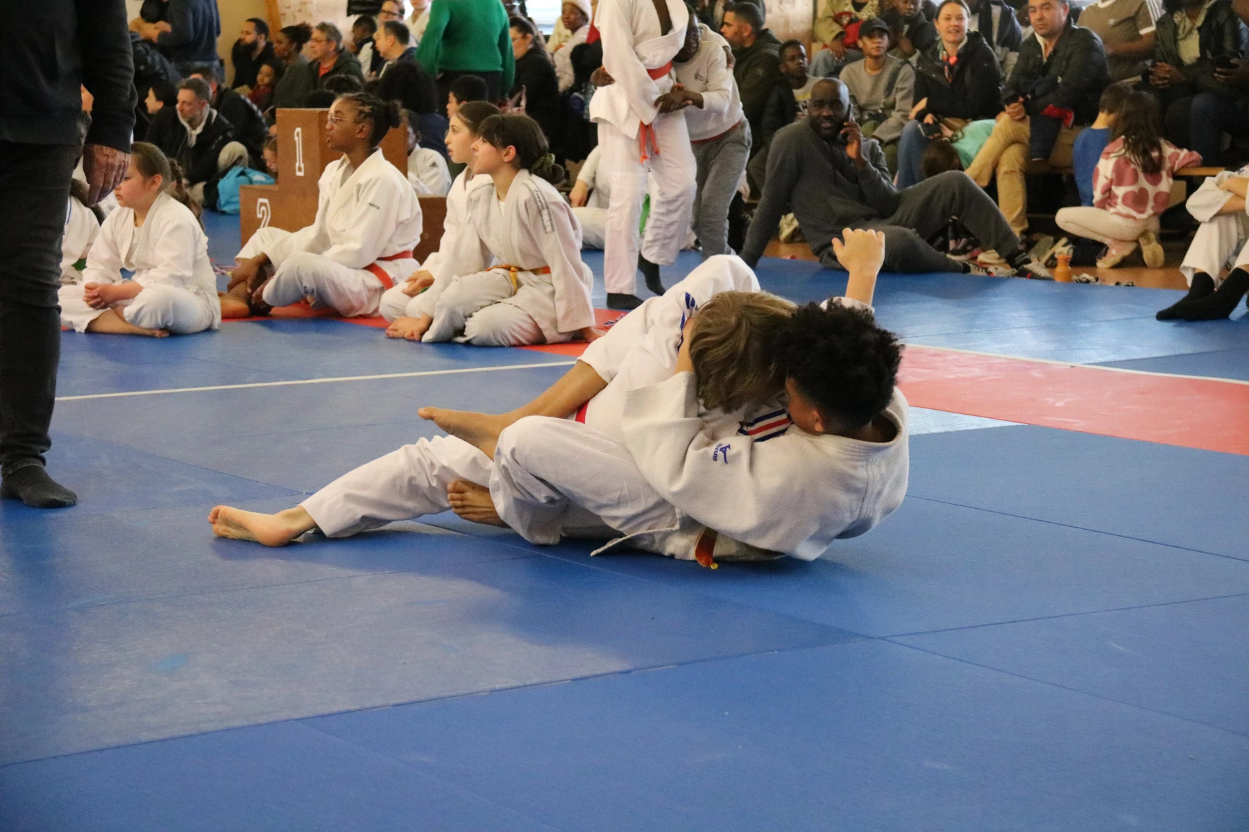 Deux petites judokas s'affrontant avec détermination lors d'un tournoi.