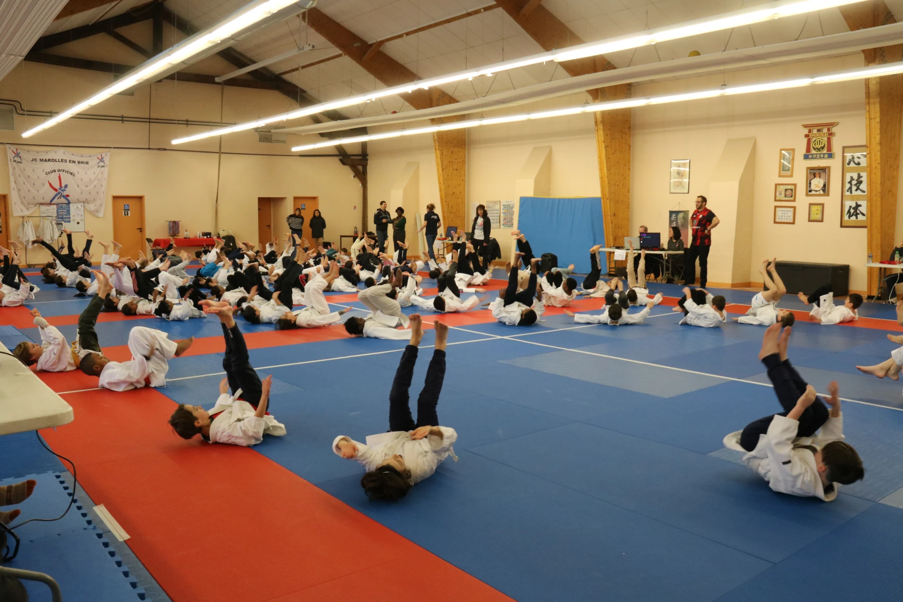 Un jeune garçon recevant sa nouvelle ceinture blanche de la part d'un instructeur, pendant que d'autres judokas et spectateurs regardent.