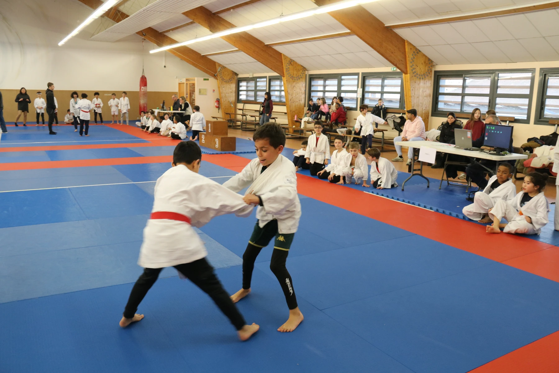 Judokas alignés avec leurs trophées, de différents âges, lors d'une remise de récompenses au dojo.