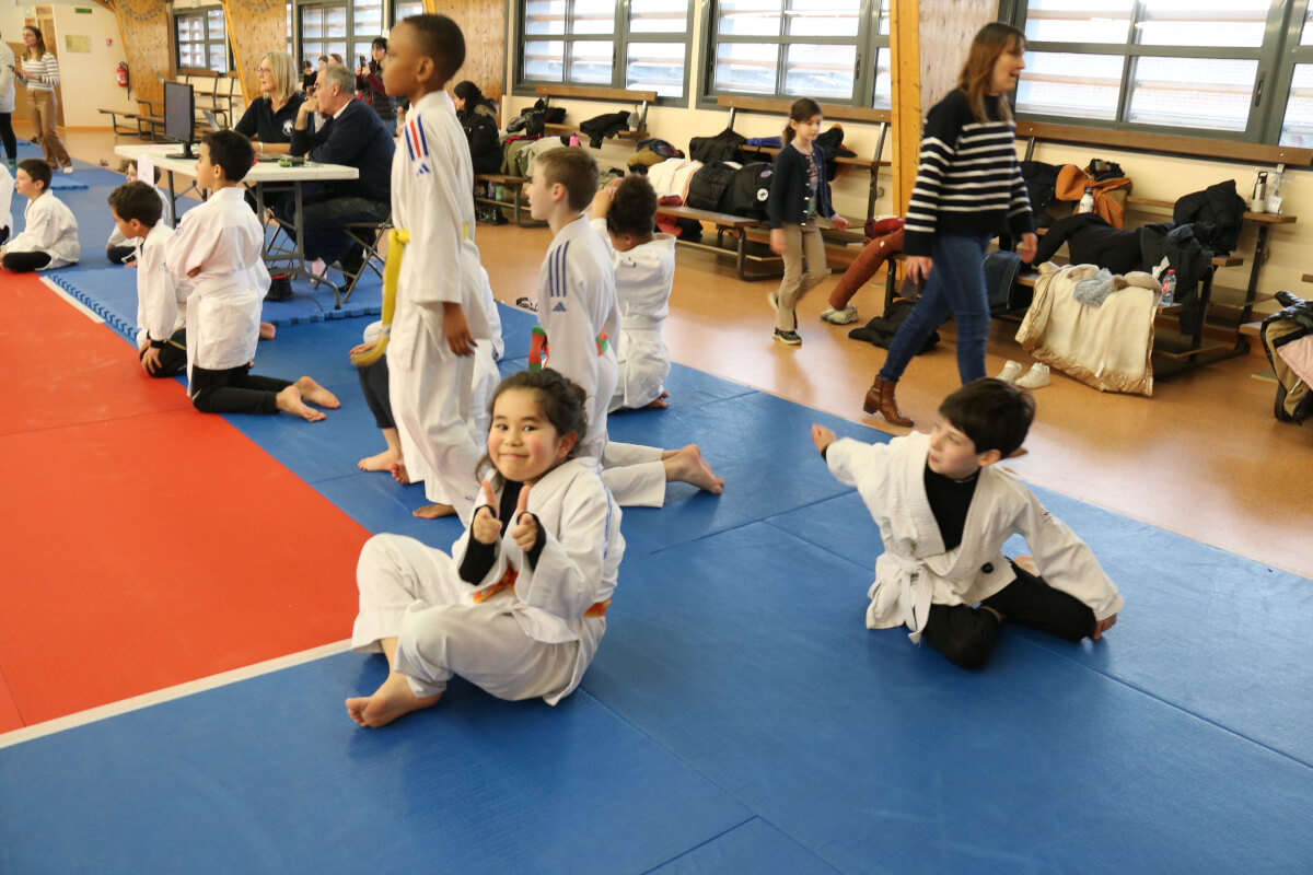 Deux judokas exécutant une technique de projection, sous le regard attentif de jeunes enfants assis au fond.