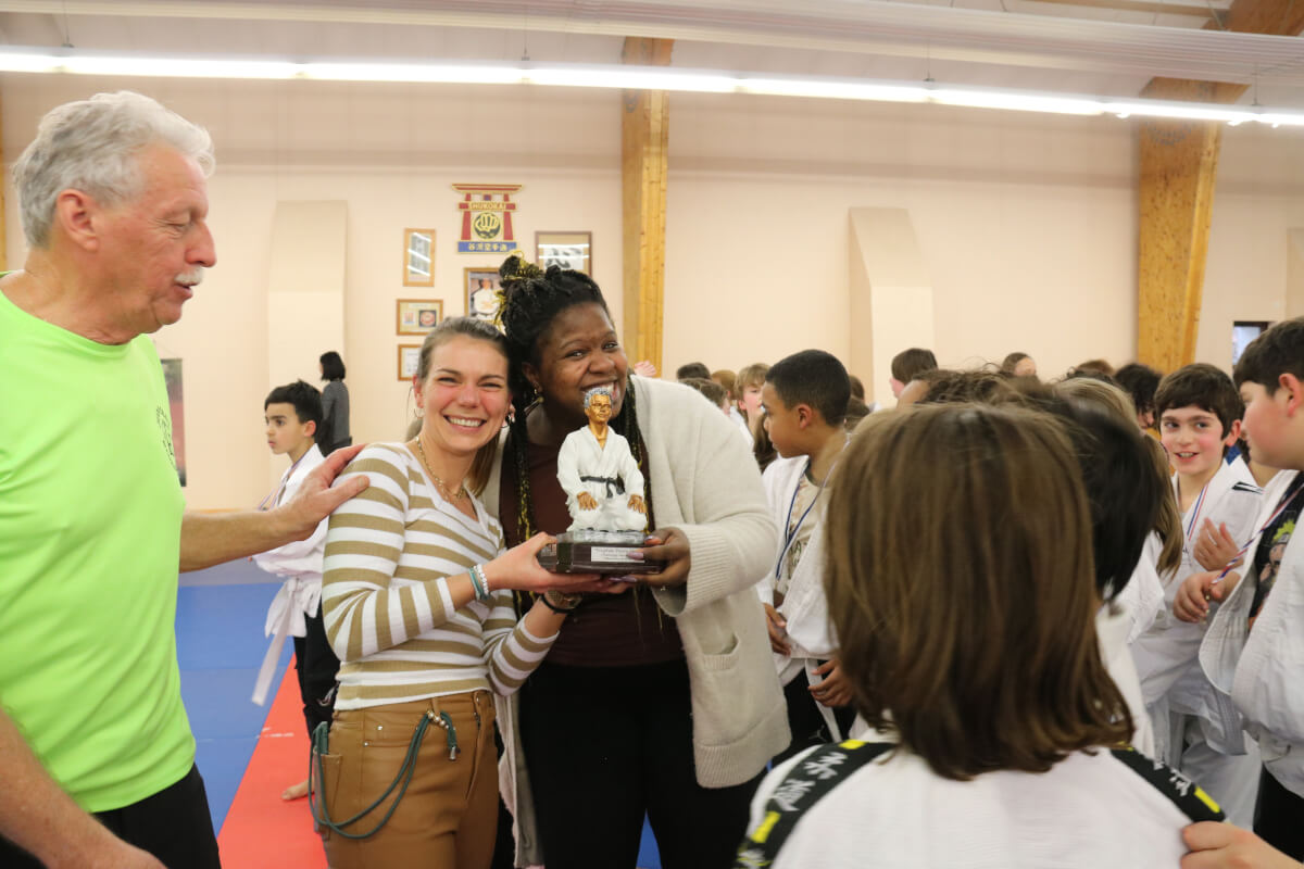 Un jeune judoka se préparant à recevoir sa nouvelle ceinture lors d'une cérémonie en présence de ses camarades et des parents.
