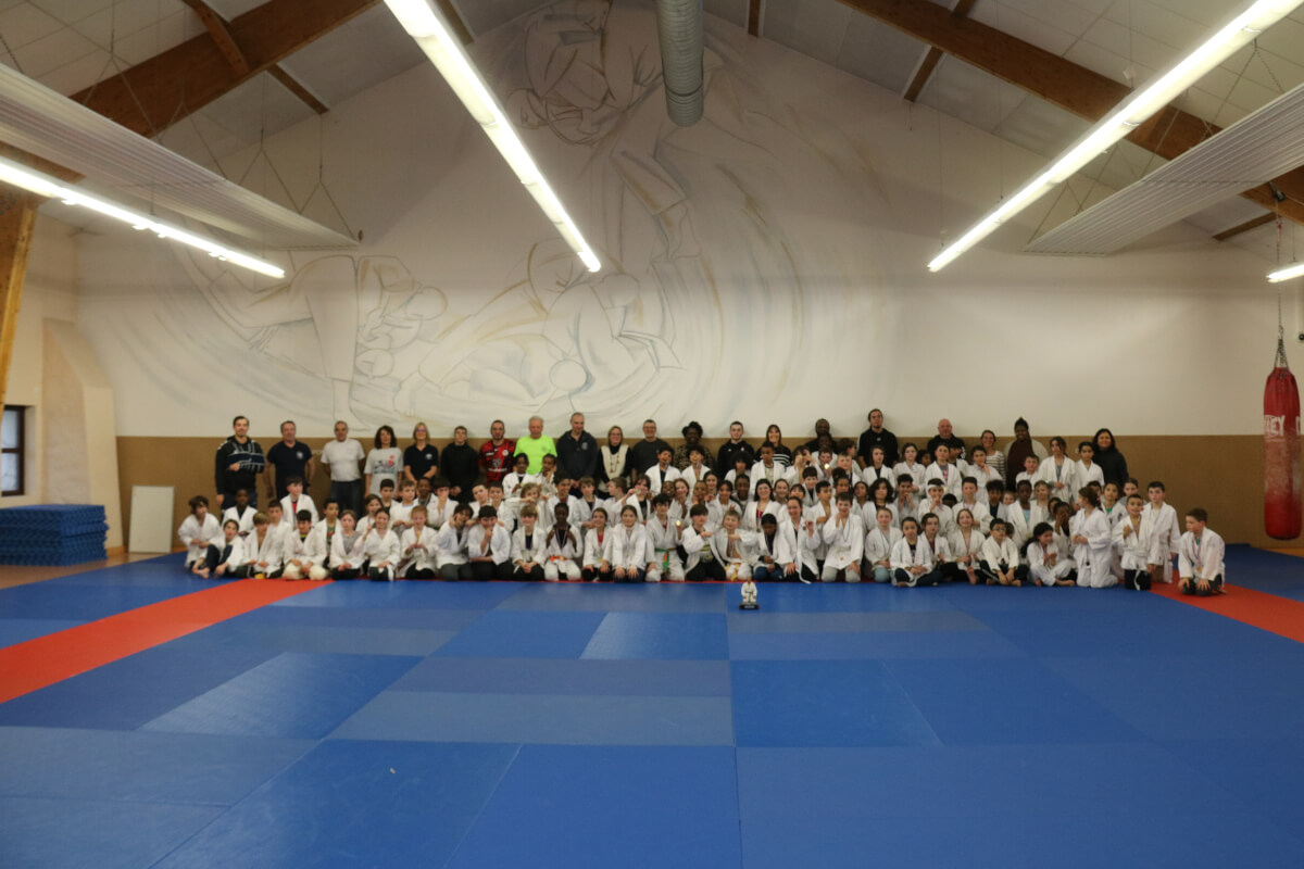 Un pratiquant de judo exécutant un mouvement de projection pendant une démonstration au dojo sous le regard des enfants assis.