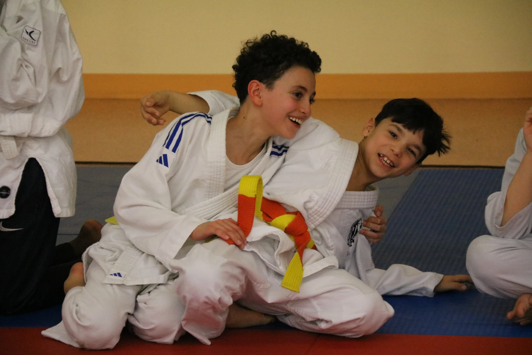 Deux jeunes judokas au sol se sourient pendant un combat amical lors du tournoi.