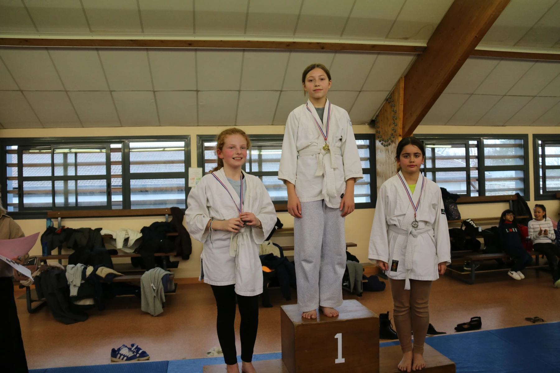 Une jeune judoka se tient debout sur la première marche du podium après sa victoire.