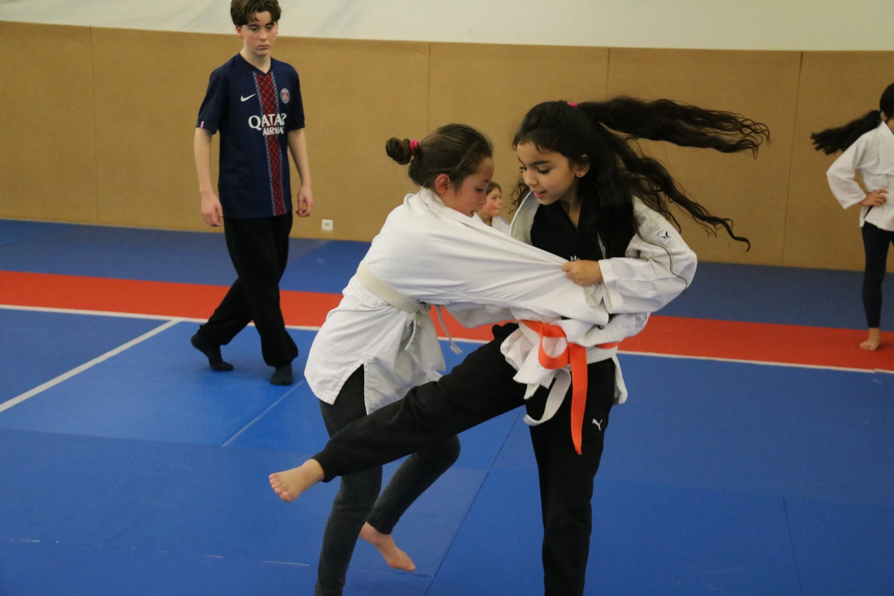 Deux jeunes judokas s'affrontent debout dans un échange dynamique, l'une saisissant fermement le kimono de l'autre.