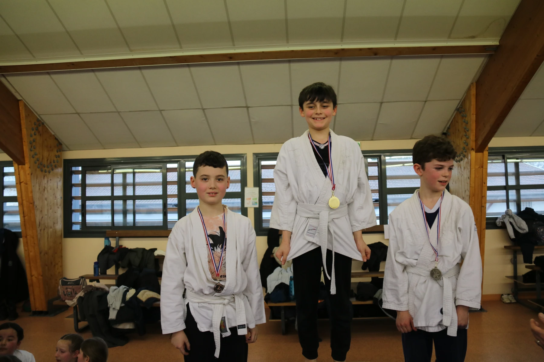 Un jeune judoka montre fièrement sa médaille, entouré de ses camarades de podium.