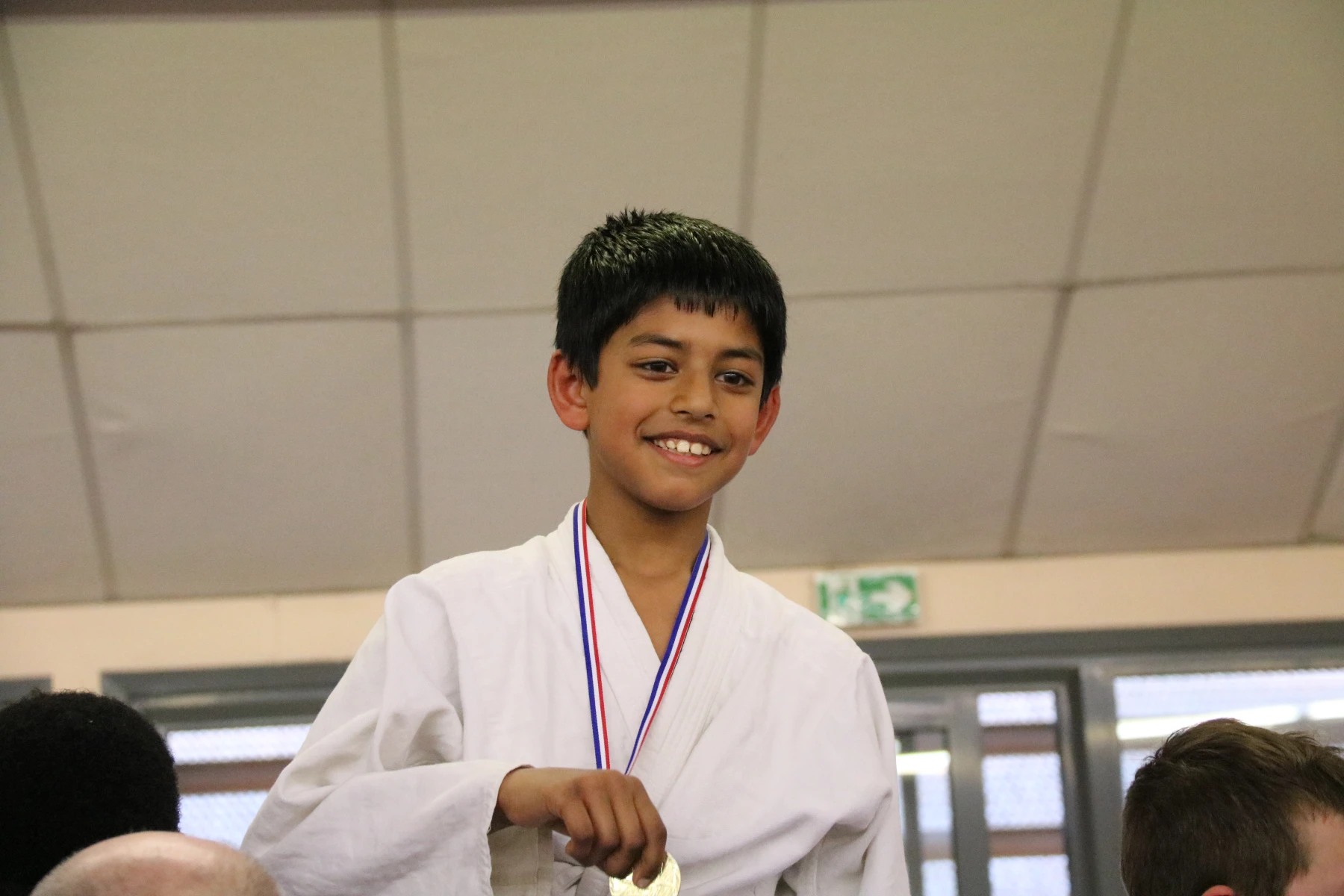 Un jeune judoka souriant mord sa médaille, fier de sa performance au tournoi.