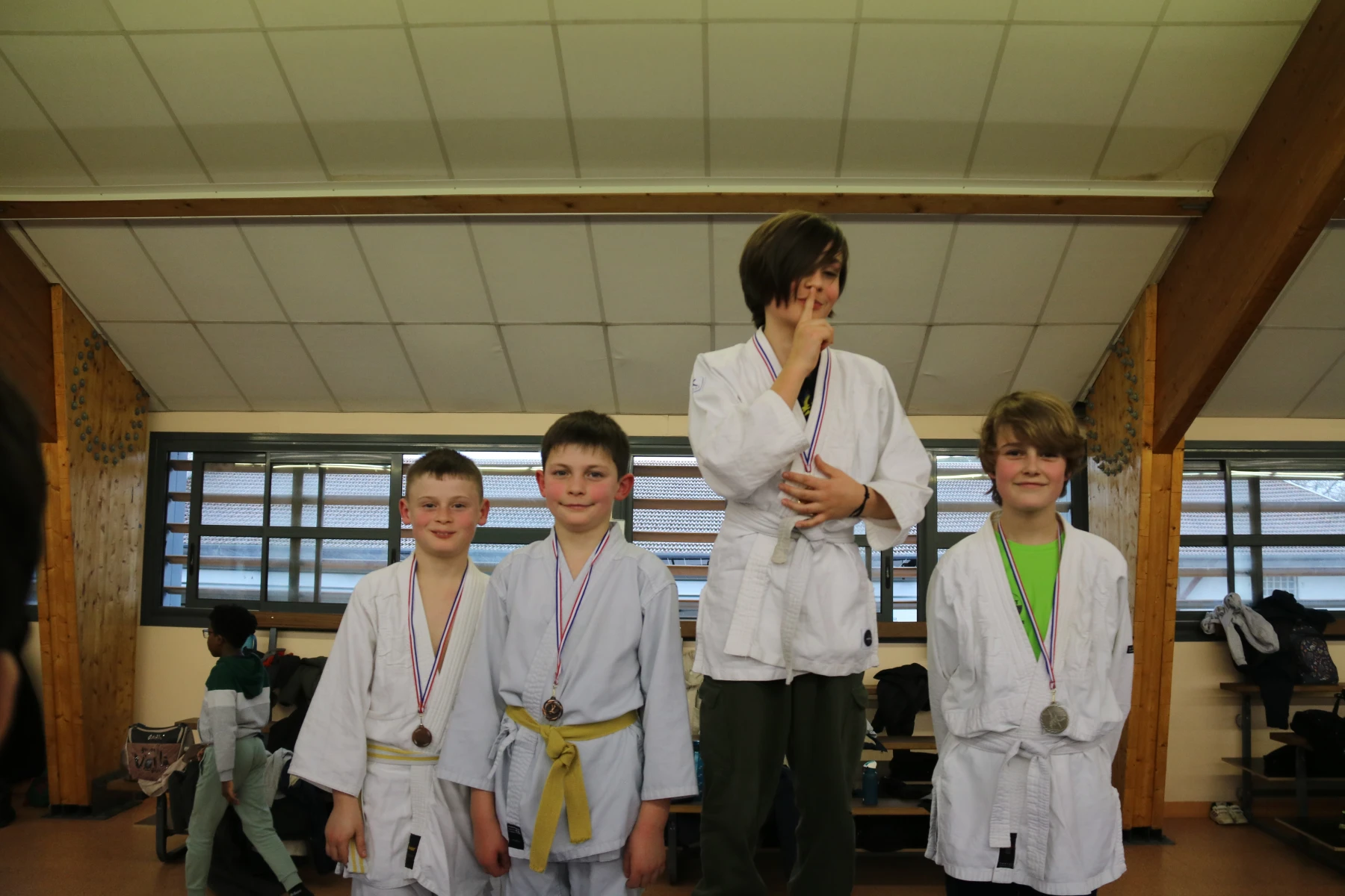 De jeunes judokas médaillés posent ensemble devant les fenêtres du dojo.